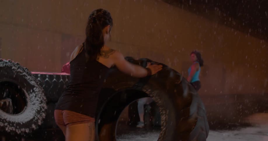 A woman is pushing a large tire in the snow