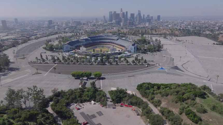 An aerial view pans over the vast, empty parking lots surrounding Dodger Stadium with the downtown Los Angeles skyline in the background