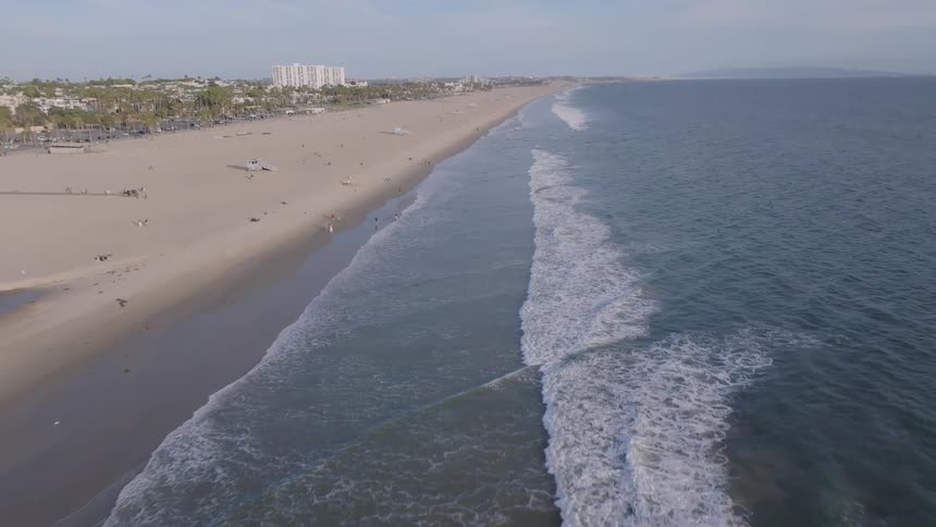 A slow aerial shot moves backward along the extensive coastline of a beautiful beach, as gentle ocean waves wash ashore