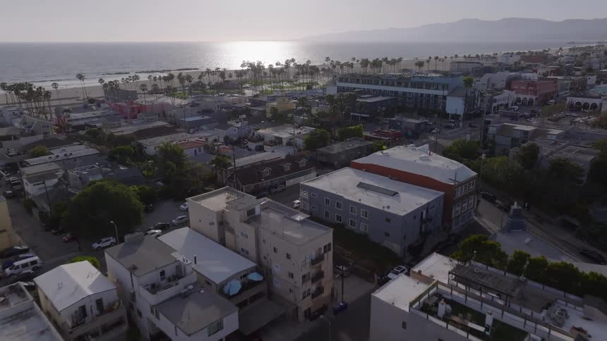 An aerial view flying over the Venice Beach neighborhood towards the Pacific Ocean at sunset