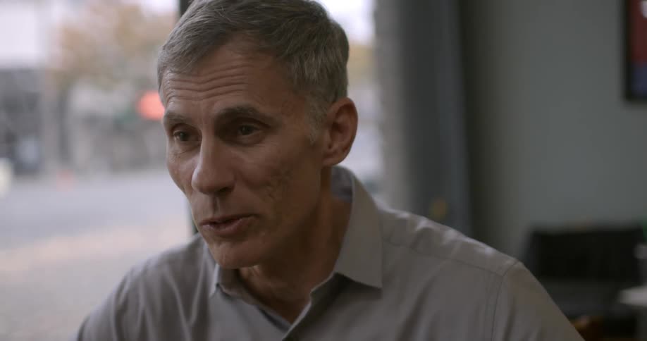 A man in a coffee shop is talking to someone across the table