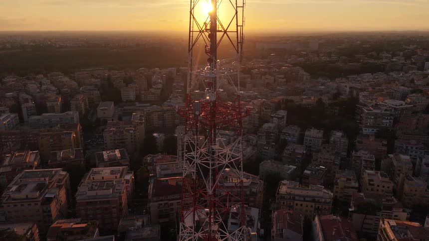 Stunning aerial view of a large telecommunications tower silhouetted against a golden sunset over a sprawling cityscape