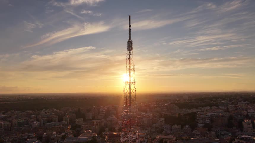 Aerial view of a tall telecommunications tower silhouetted against a beautiful golden sunset over a sprawling city