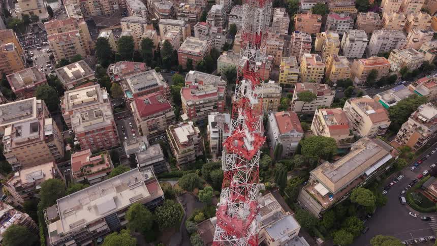 Aerial shot starting with a wide view of a city and tilting down to a top-down perspective of a large red and white telecommunications tower