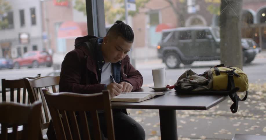 A man writes in a notebook while sitting in a coffee shop