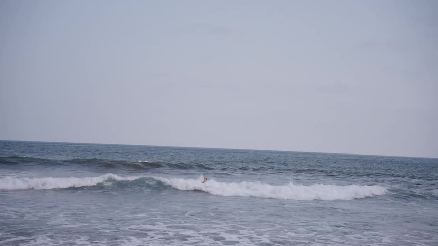 A group of people enjoy swimming and surfing in the ocean on an overcast day in slow motion