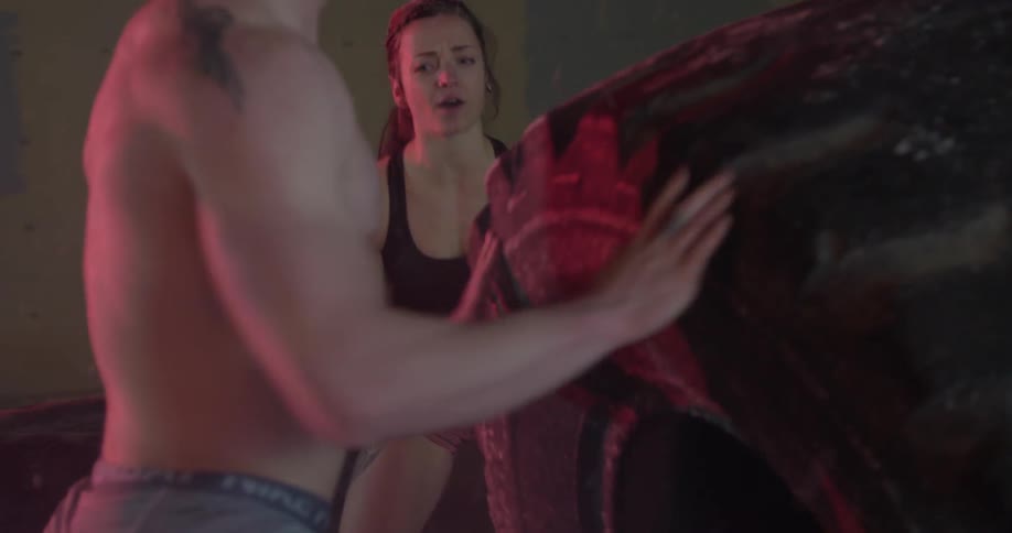 A young man and woman are strength-training outdoors in the snow by flipping large tires