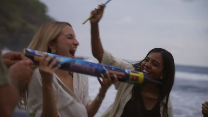 A group of diverse friends joyfully dance and play with fireworks on a dark sand beach in slow motion