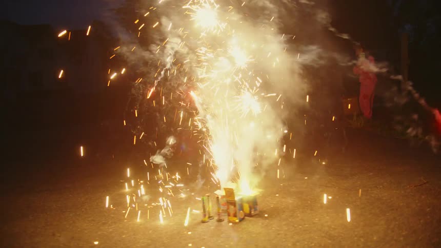 Colorful fountain fireworks erupt with sparks and smoke on a driveway at night during a family celebration