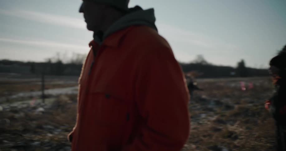 A farmer and a woman walk through a frosty field on a cold morning, revealing a flock of sheep grazing peacefully in the background