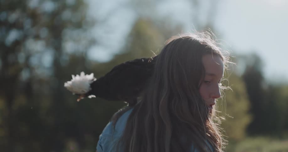 A white-crested Polish chicken perched on a young girl's shoulder flies away in slow motion in a sunny backyard