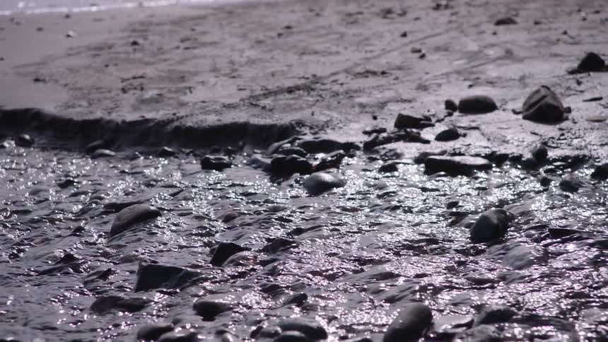 A gentle stream flows over shimmering pebbles on a sandy beach and into the ocean