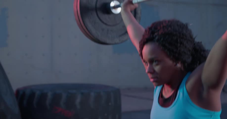 A woman lifts up a large weight above her head