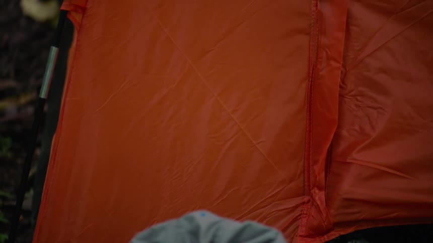 A close-up panning shot captures raindrops hitting a bright orange tent during a rainy day in the forest