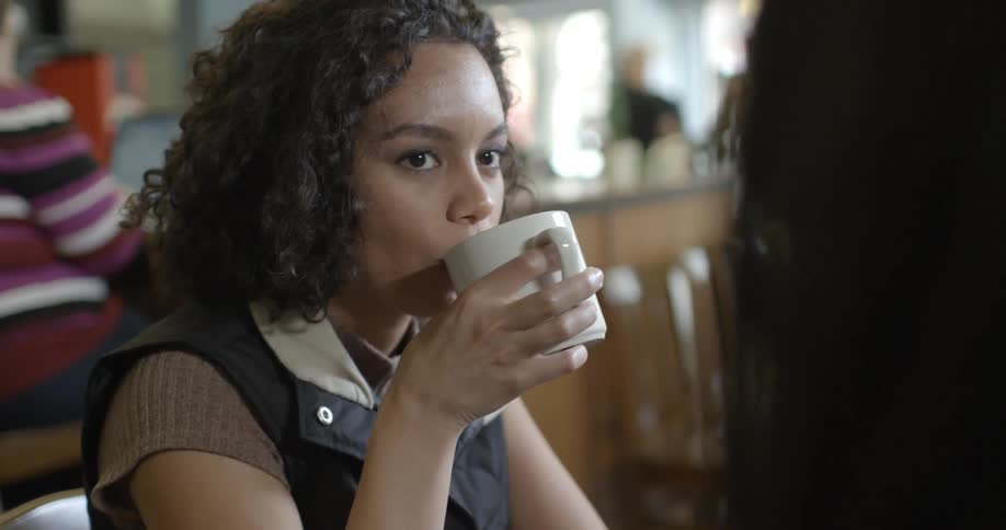A woman drinks from a mug while sitting in a coffee shop