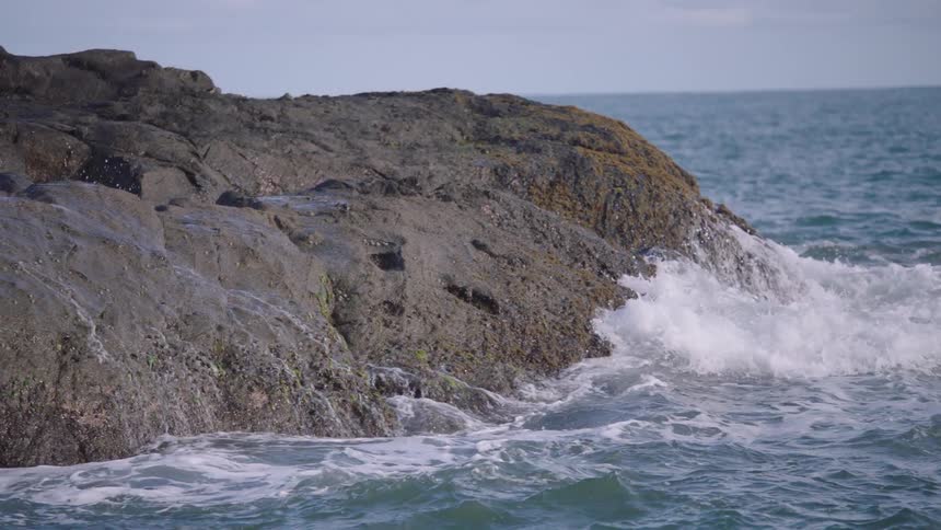 Powerful ocean waves crash against rugged coastal rocks in dramatic slow motion