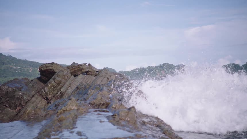 Dramatic slow-motion footage of powerful ocean waves crashing against a rugged, rocky coastline