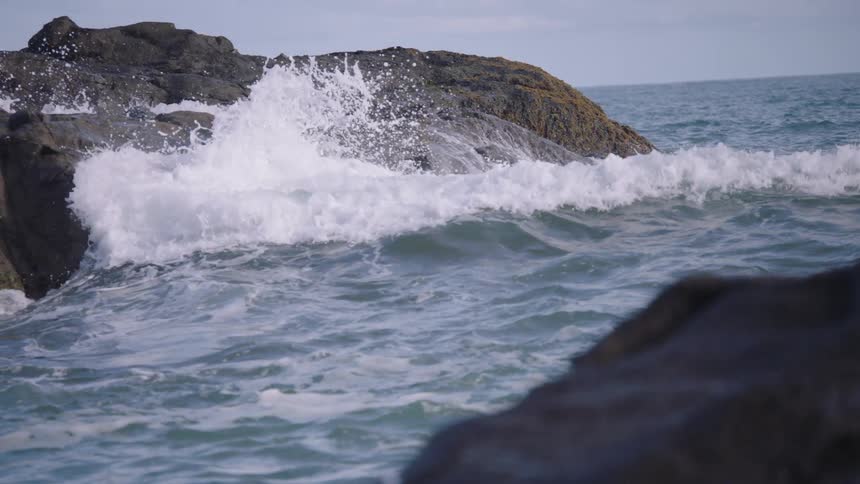 Slow motion shot of a powerful ocean wave crashing against a rugged, rocky coastline