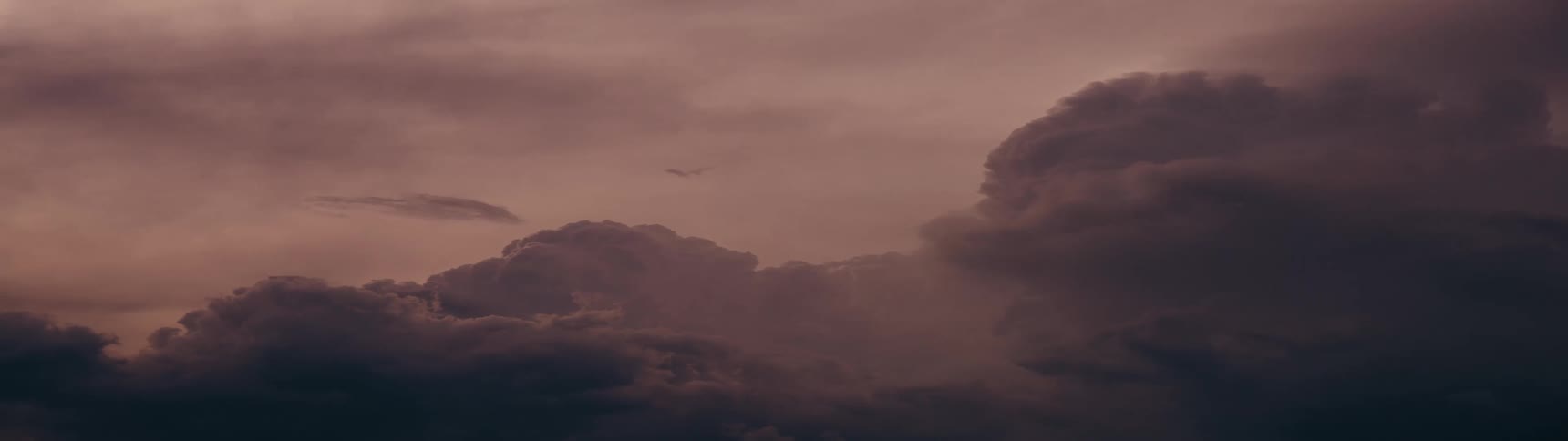 Dark, ominous clouds drift across a somber sky as a distant airplane passes by