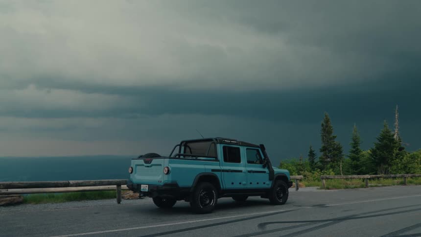 Lightning strikes in the ominous storm clouds behind a blue pickup truck parked on a scenic mountain road
