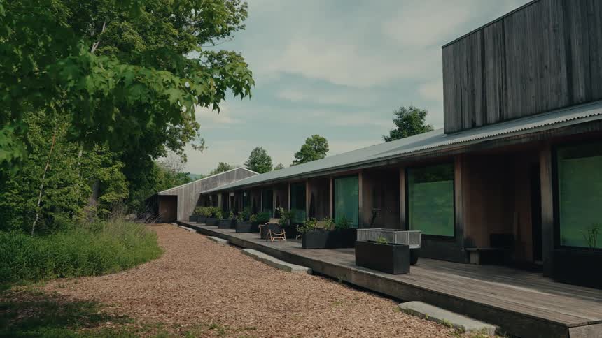 The serene exterior of a modern wooden building with a long deck sits peacefully in a lush, natural landscape