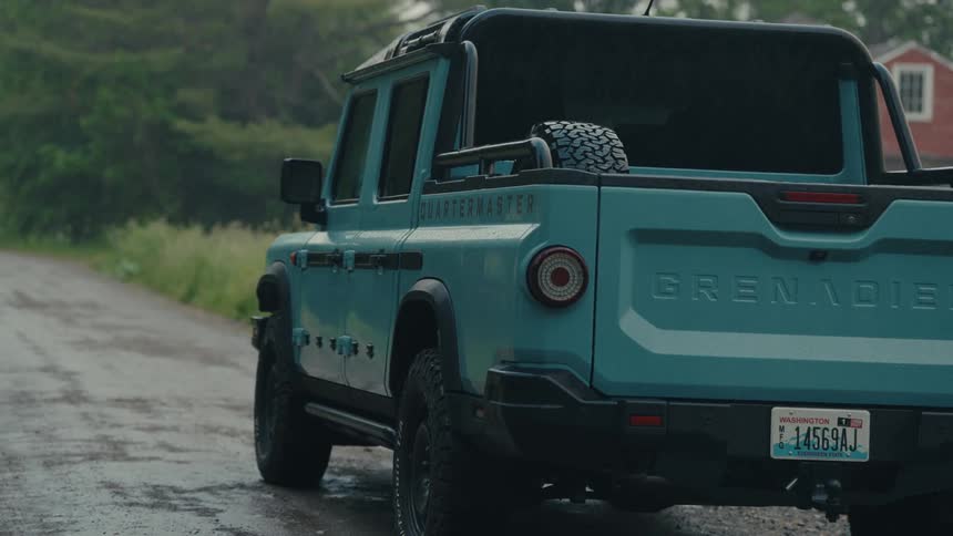 A close-up of a light blue pickup truck parked on a wet country road during a gentle rain shower
