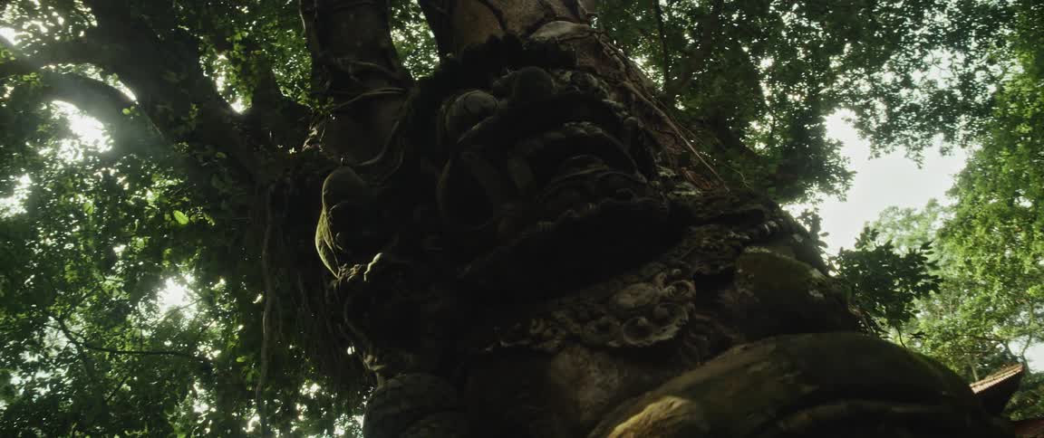 An ancient, moss-covered stone deity statue is revealed, overgrown by the roots of a giant jungle tree