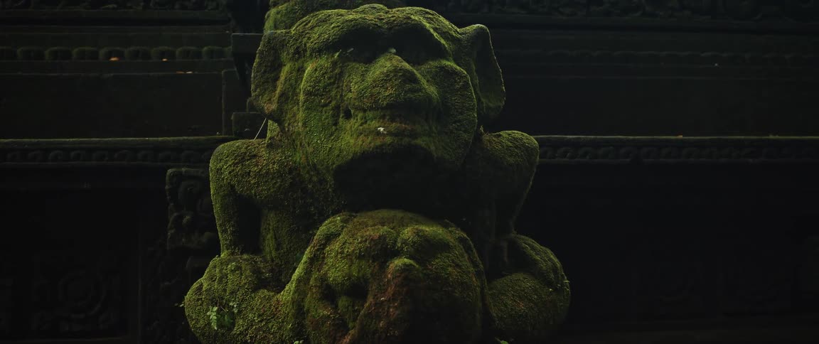 A slow pan across an ancient stone statue of a mythical creature completely covered in green moss