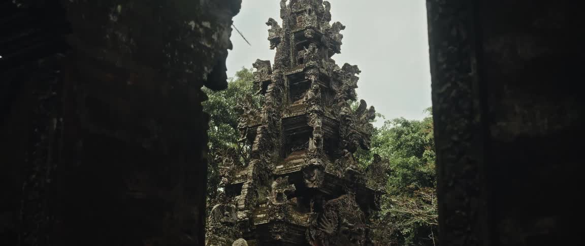 A slow zoom out reveals the intricate stone carvings of an ancient Balinese temple gate surrounded by lush jungle foliage