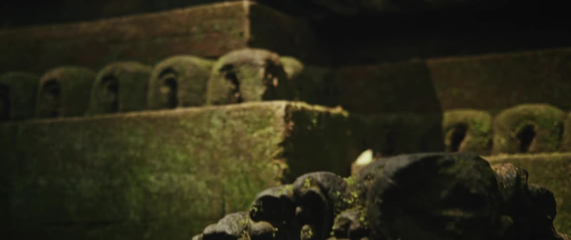 An ancient stone statue covered in green moss reveals intricate details in a slow, dramatic close-up shot