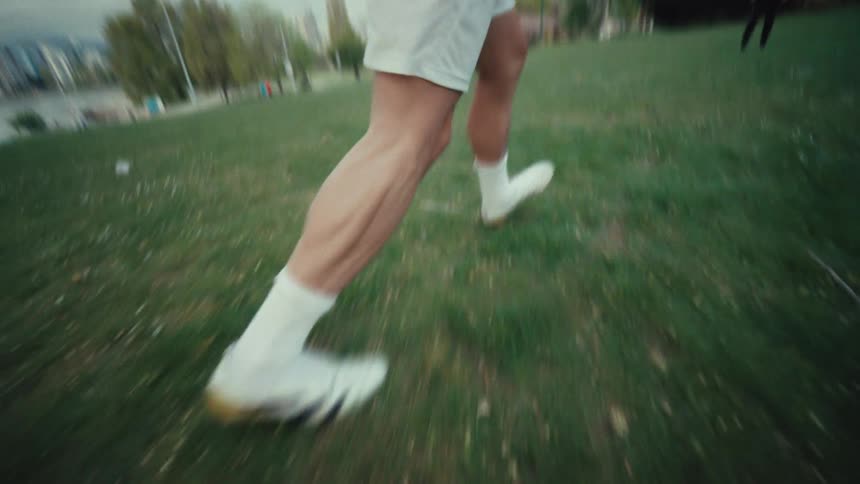 Dynamic low-angle slow-motion shot of a footballer's cleats as they dribble and juggle a soccer ball on a grassy field
