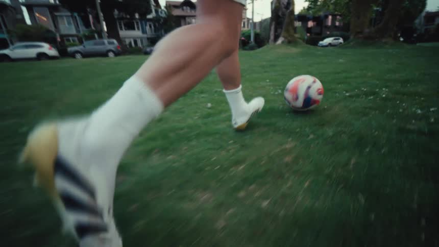 Slow motion close-up of a soccer player's feet skillfully dribbling a ball across a grassy park