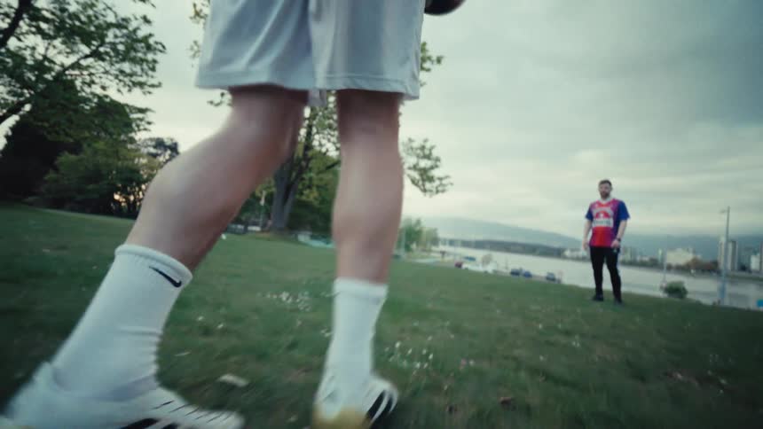 A slow-motion, close-up, low-angle shot of a soccer player's legs as he juggles a ball on a grassy field in a park