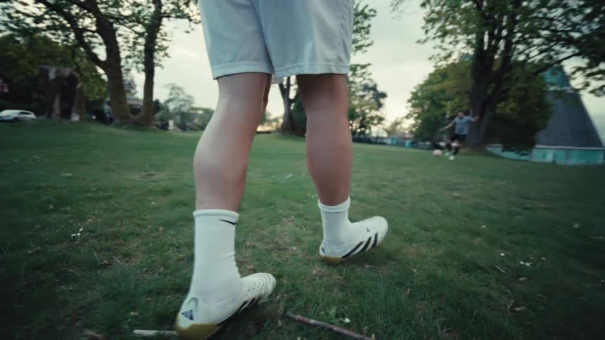 Close-up slow-motion tracking shot of a soccer player's legs and cleats running across a grassy park before dribbling and kicking the ball
