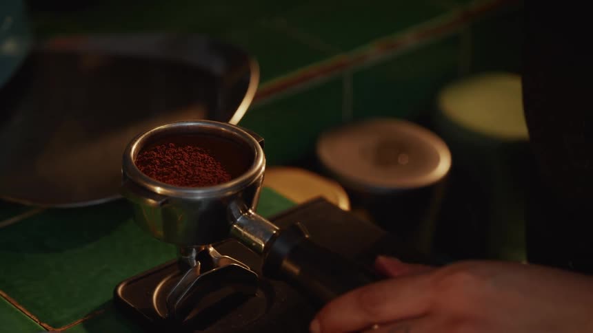 A close-up of an espresso portafilter filled with fine coffee grounds on a green tiled counter