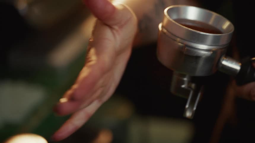 Close up slow motion of a barista grinding coffee beans and tamping the grounds in a portafilter to make espresso