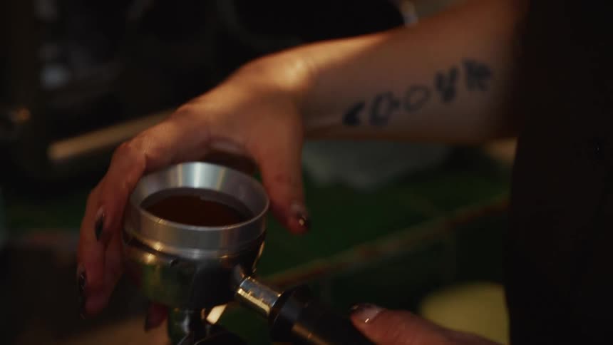 Slow motion close-up of a tattooed barista carefully leveling coffee grounds in a portafilter before making espresso