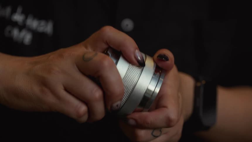 Slow-motion close-up of a barista with tattoos and stylish nails using a manual coffee grinder