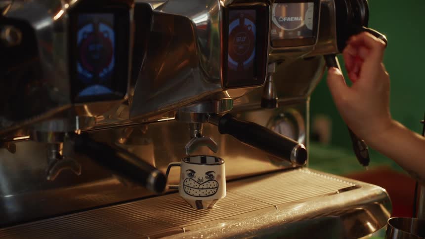 A barista programs a professional espresso machine to brew a coffee in a quirky smiling mug