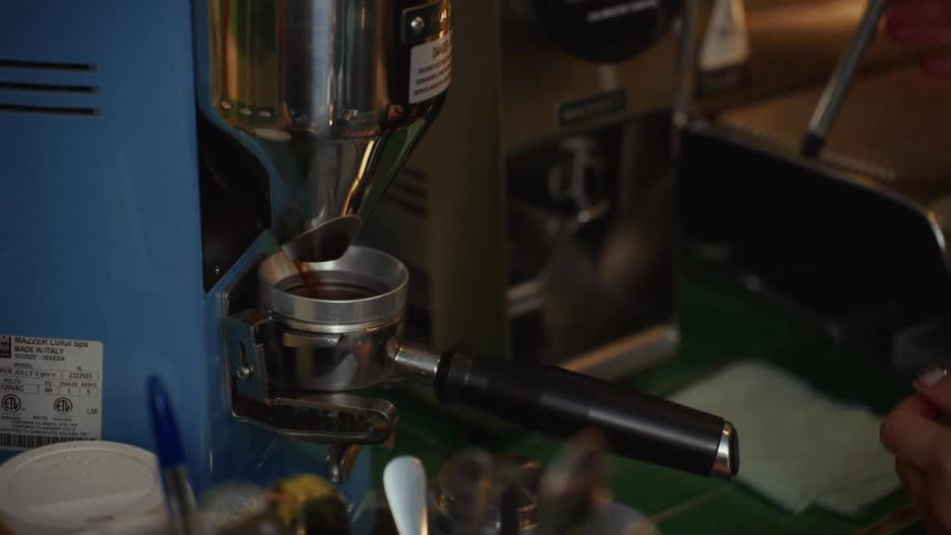 Close up slow motion of a tattooed barista grinding fresh coffee beans into a portafilter
