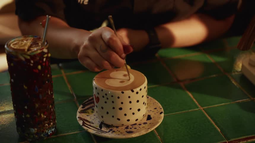 A barista carefully etches a cute ghost design into the foam of a specialty coffee drink in a polka-dot mug