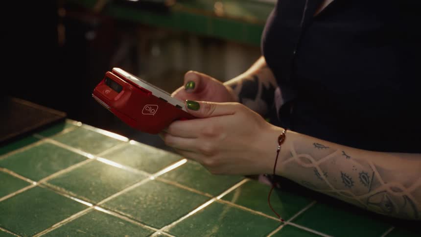 A close-up shot of a tattooed bartender entering the payment amount on a red credit card terminal at a bar counter