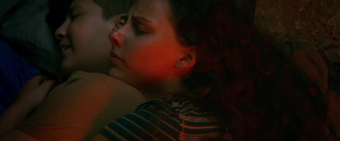 A distressed woman and her young son huddle together, seeking comfort and warmth in a dimly lit, dark space