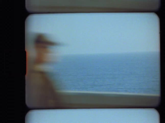 Super 8mm film shows a serene ocean view as a blurry figure in a hat walks past