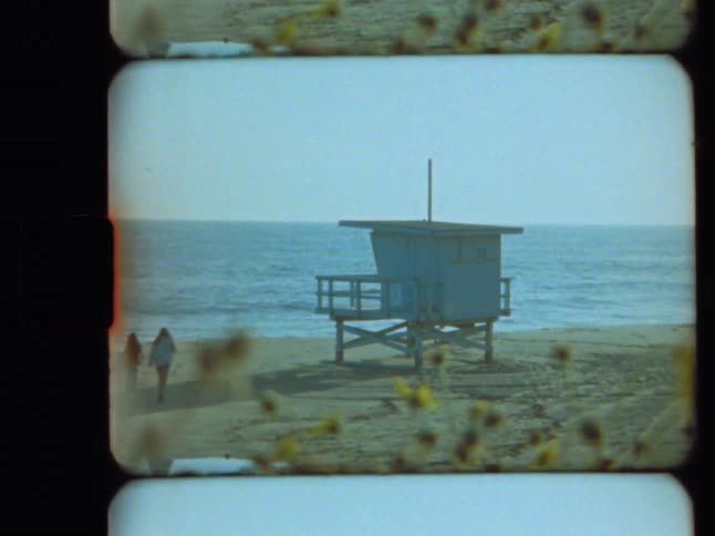 A lifeguard tower stands on a California beach with wildflowers in the foreground in a nostalgic Super 8 film shot