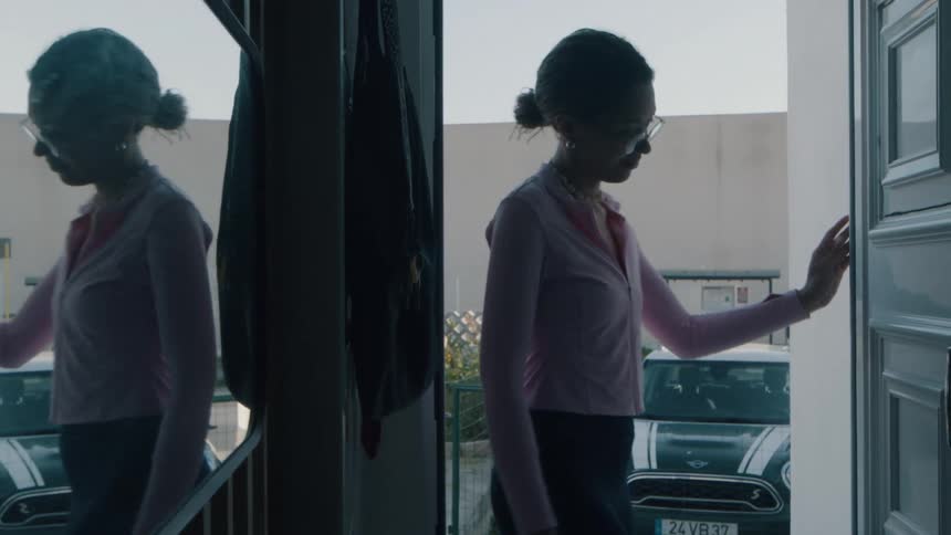 A young woman in silhouette looks out her front door, smiles, and then closes it to return inside