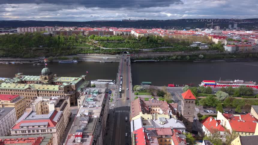 Static high-angle view of Prague's cityscape with the Stefanik Bridge crossing the Vltava River under a dramatic, cloudy sky