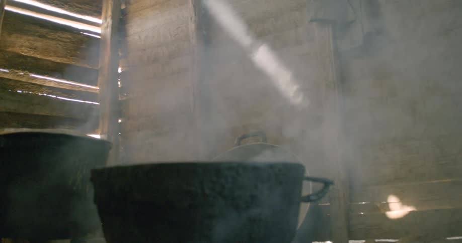 A dramatic beam of light illuminates steam rising from cooking pots in a rustic wooden kitchen