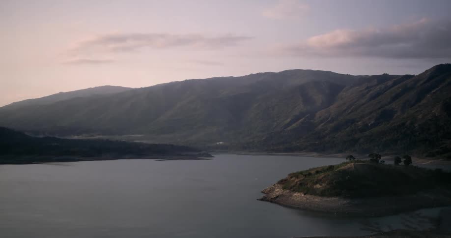 A picturesque mountain lake is revealed from behind passing foliage during a tranquil sunrise