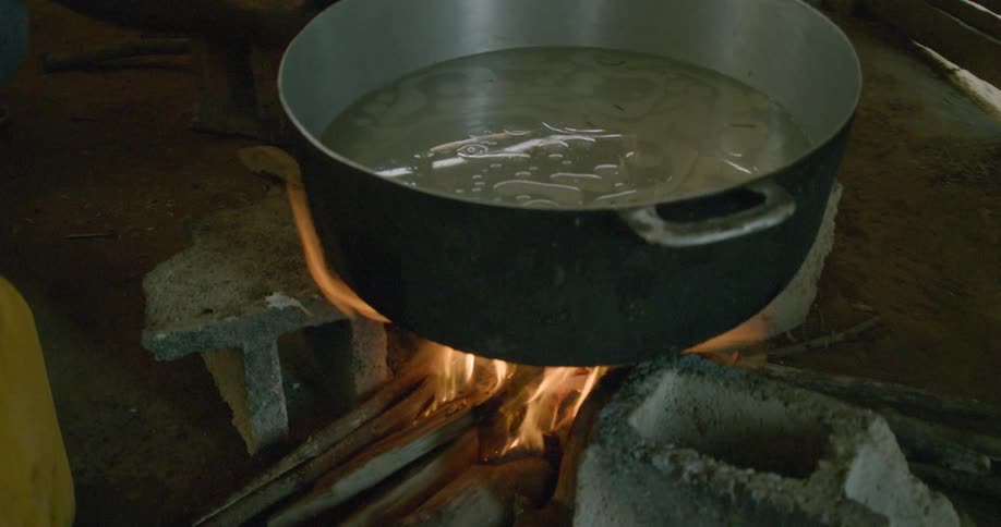 A large pot of food boils over a primitive campfire stove made of cinder blocks